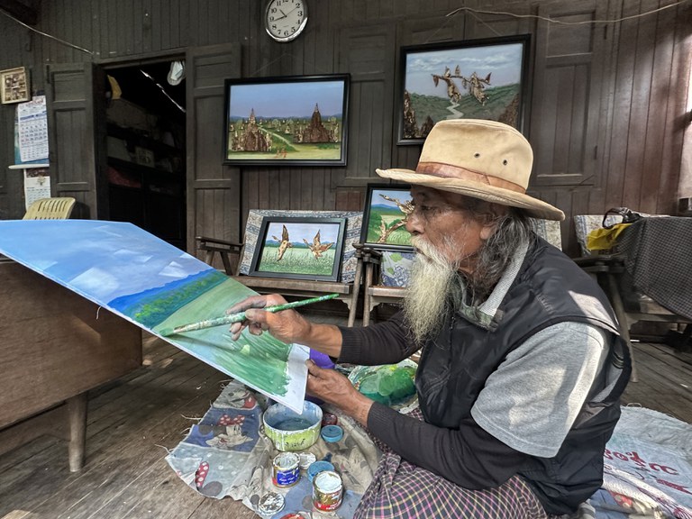 သစ်ခေါက်များနှင့် ပန်းချီကားဖန်တီးသည့် ဦးသန်းလှအောင်အား ၂၀၂၃ ခုနှစ် ဒီဇင်ဘာလ ၂၇ ရက်နေ့က မန္တလေးမြို့ အောင်မြေသာစံမြို့နယ်ရှိ နေအိမ်တွင် တွေ့ရစဉ်။ (Photo: RFA)