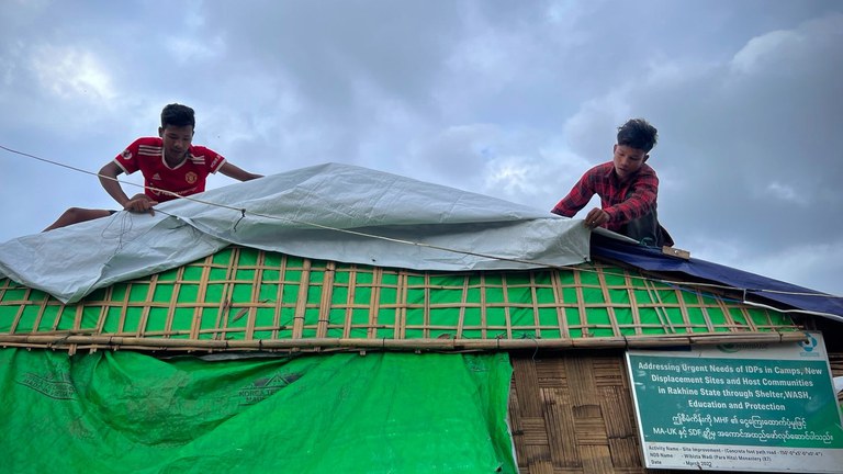 စစ်တွေမြို့ပေါ်က ဝိဘဇ္ဇဝါဒီ စစ်ဘေးဒုက္ခသည်စခန်းမှာ ခိုလှုံနေသူ နှစ်ဦး အိမ်အမိုးပြင်ဆင်နေတာကို ၂၀၂၃ ခုနှစ် ဇွန်လ ၉ ရက်နေ့က တွေ့ရစဉ်။ (Photo : RFA)