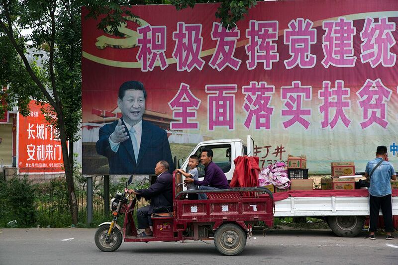 河南省平顶山市居民经过习近平的海报和“积极发挥党的建设引领作用,全面实施脱贫攻坚计划”的部分标语。(美联社)