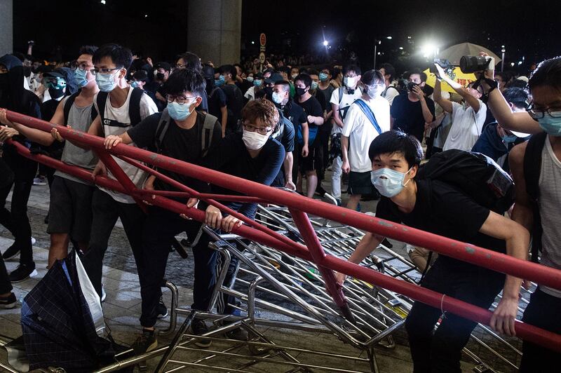 2019年6月10日凌晨12点,一批戴上口罩和面罩的示威者手挽手闯进香港立法会示威区,推倒铁马,推向警察防线。(法新社)