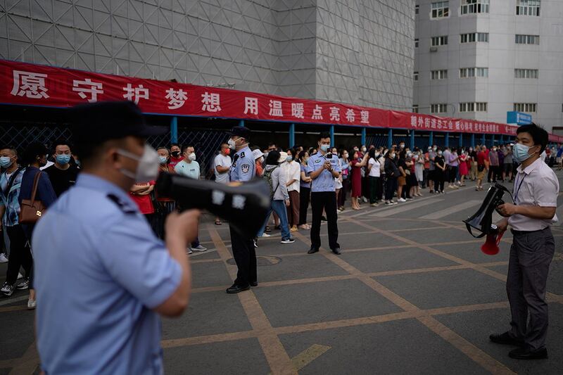 2022 年 6 月 7 日,在北京举行的中国全国高考第一天,警察,学校官员与学生家长在学校外。(美联社)