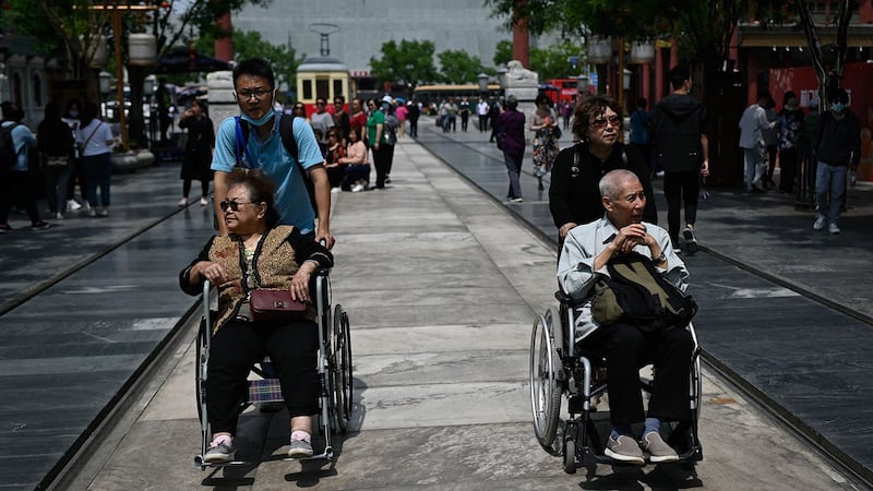 2021年5月11日,在北京的一条街道上,一名老年男女坐着轮椅。 (法新社)