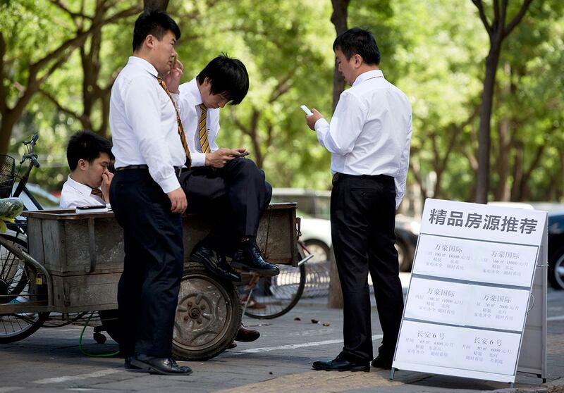 在北京,房地产销售人员等待潜在买家时,在显示待售和出租物业的展示板附近查看他们的智能手机。(美联社)