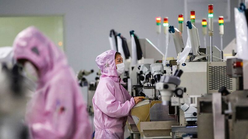 2020 年 2 月 16 日,员工戴着口罩和防护服在江苏省泗洪市的一条智能芯片生产线上工作。(法新社)